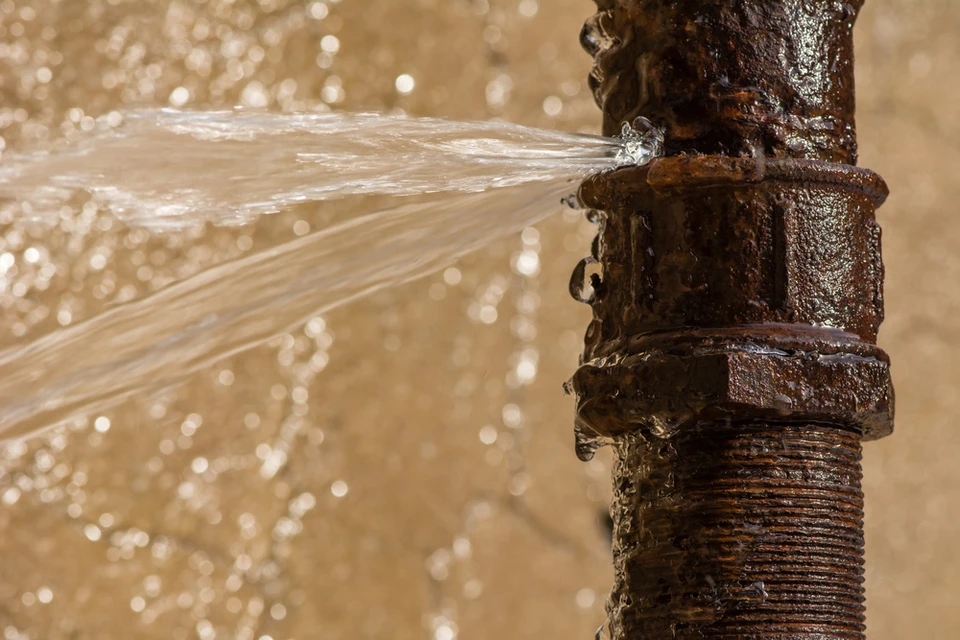 Fuite d'eau majeure sur canalisation extérieure, jet d'eau sous pression s'échappant d'un raccord de tuyauterie métallique corrodé